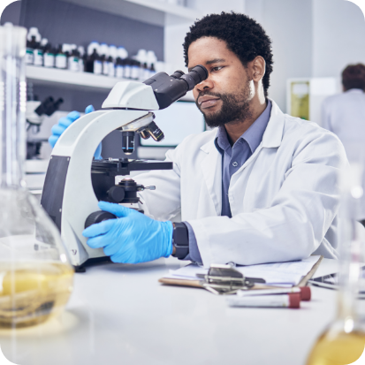 A man looking into a microscope while wearing blue gloves.